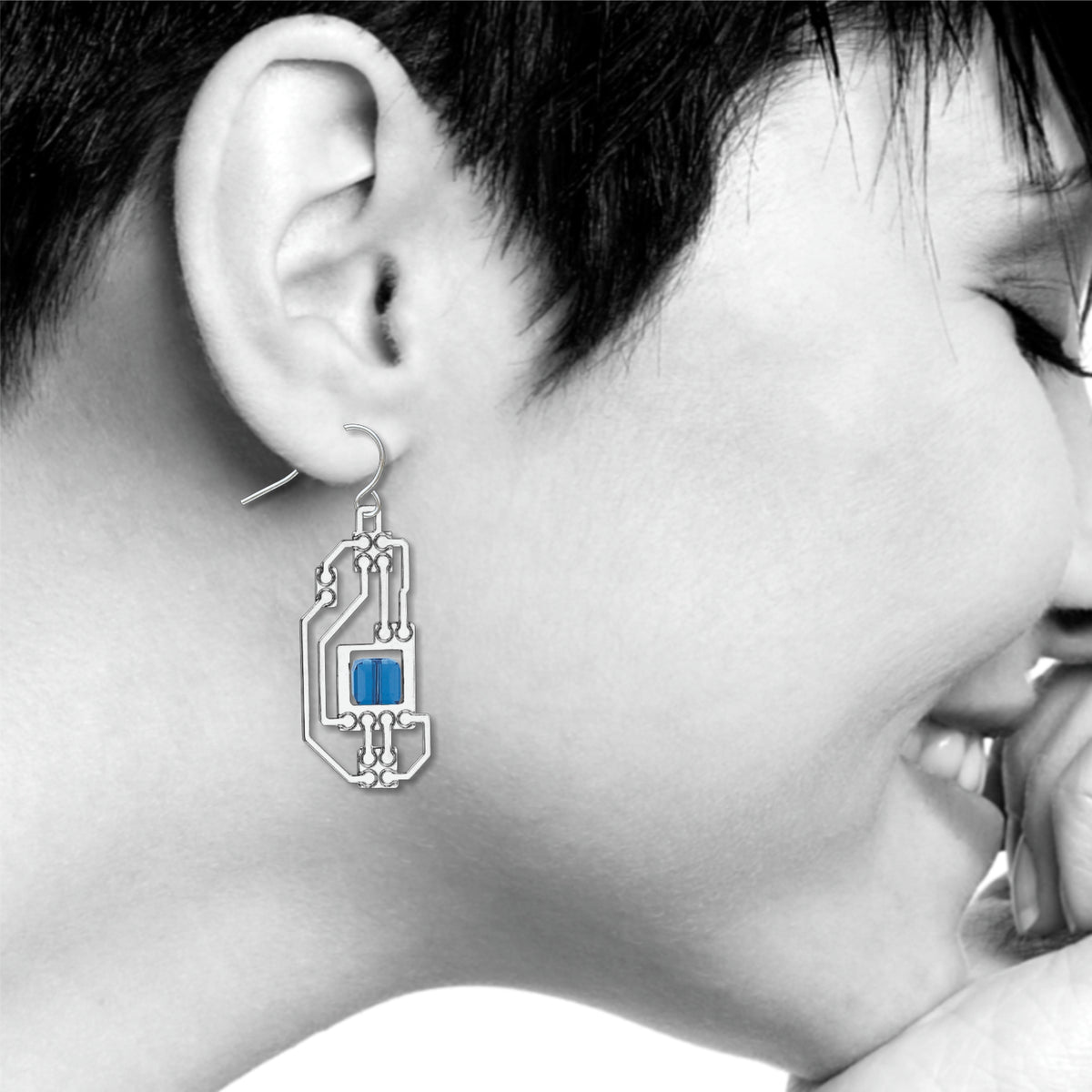 Silver circuit-inspired drop earring with blue geometric accent stone worn on ear.