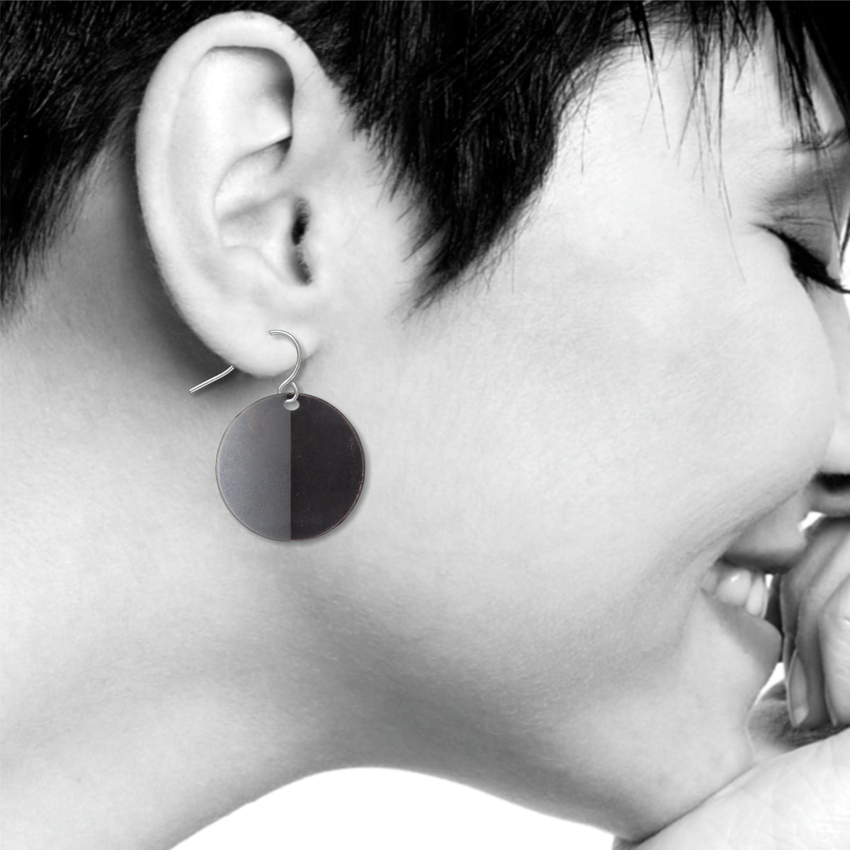 An Orb circular drop earring with a bold split-tone black and gray finish, shown worn on ear with a sleek minimalist modern art-inspired design