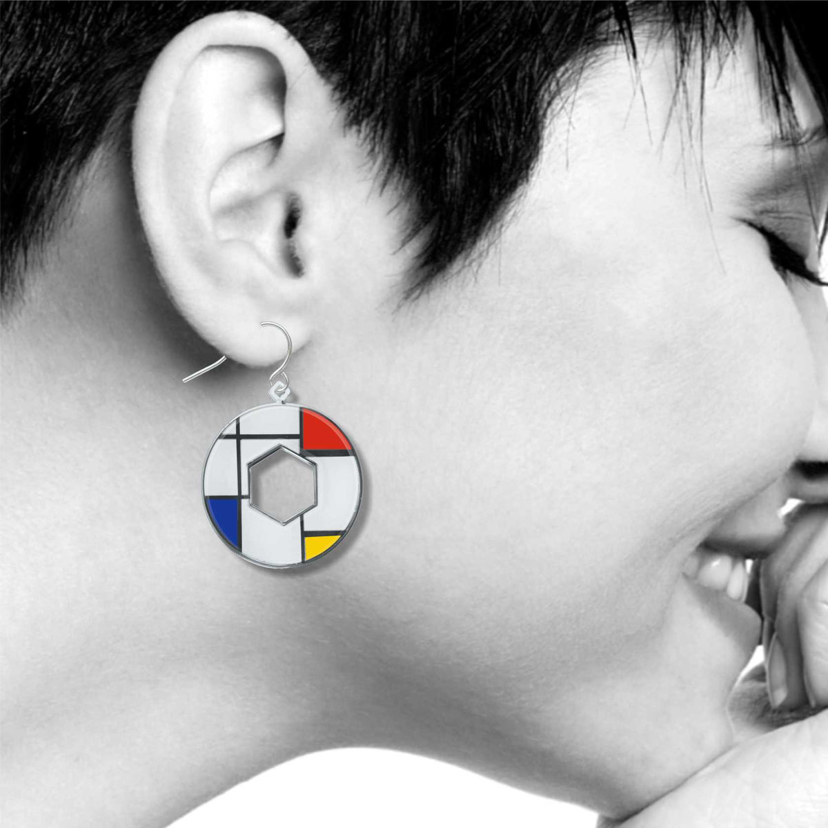 Model wearing a Utopia geometric dangle earring inspired by Mondrian artwork, featuring bold red, blue, yellow, black, and white enamel accents in a circular open-center design.