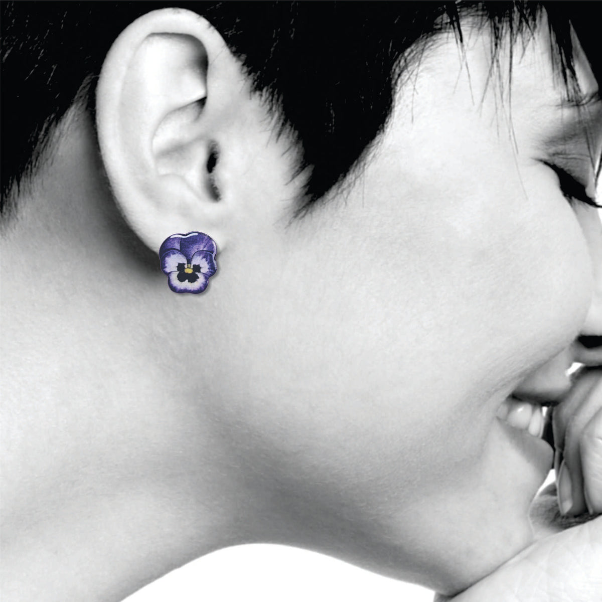 Close-up of a person wearing purple pansies flower earrings with a black and white background
