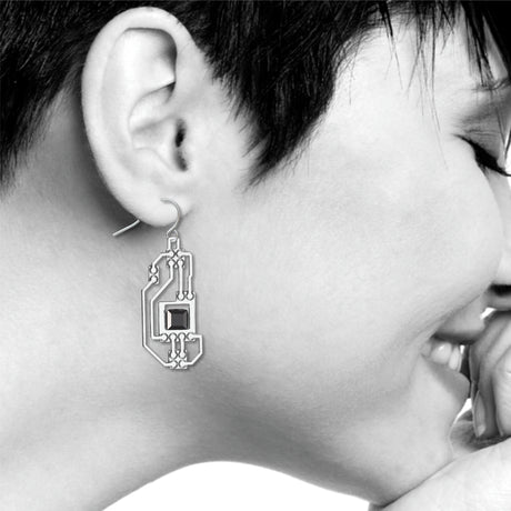 Circuits abstract silver drop earring worn on ear with intricate circuit board-inspired detailing and a faceted black geometric accent in a modern industrial design