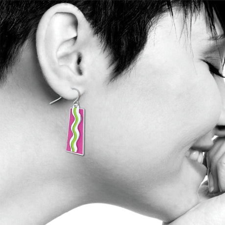 Model wearing a Matisse & the Fauves rectangular drop earring featuring vibrant pink enamel with flowing white and green wave designs inspired by Henri Matisse’s Fauvist artwork.