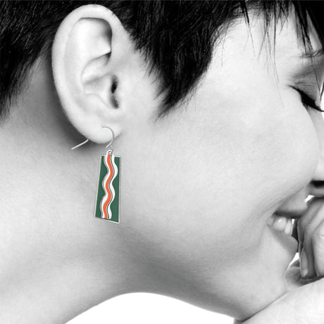 Model wearing a Matisse & the Fauves rectangular drop earring featuring flowing orange and white wave designs on a deep green enamel background inspired by Henri Matisse’s Fauvist color palette.