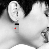 Model wearing balance earring featuring a geometric silver rectangle with a black top and red accent block.