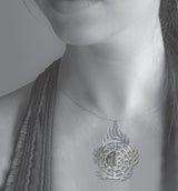 Halo of Flames Necklace worn on a silver chain, featuring a circular silver pendant with flame-like edges, geometric cutouts, and crystal accents displayed against the neckline of a model.