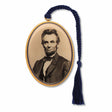 A metal bookmark featuring a portrait of Abraham Lincoln, with a tassel and gold-plated edges, with braided black tassel.