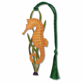 A metal bookmark in the shape of a seahorse with a green tassel, orange brood pouch holding on green sea grass with green braided tassel..
